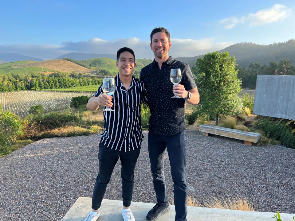 Two students hold up wineglasses outside in a vineyard