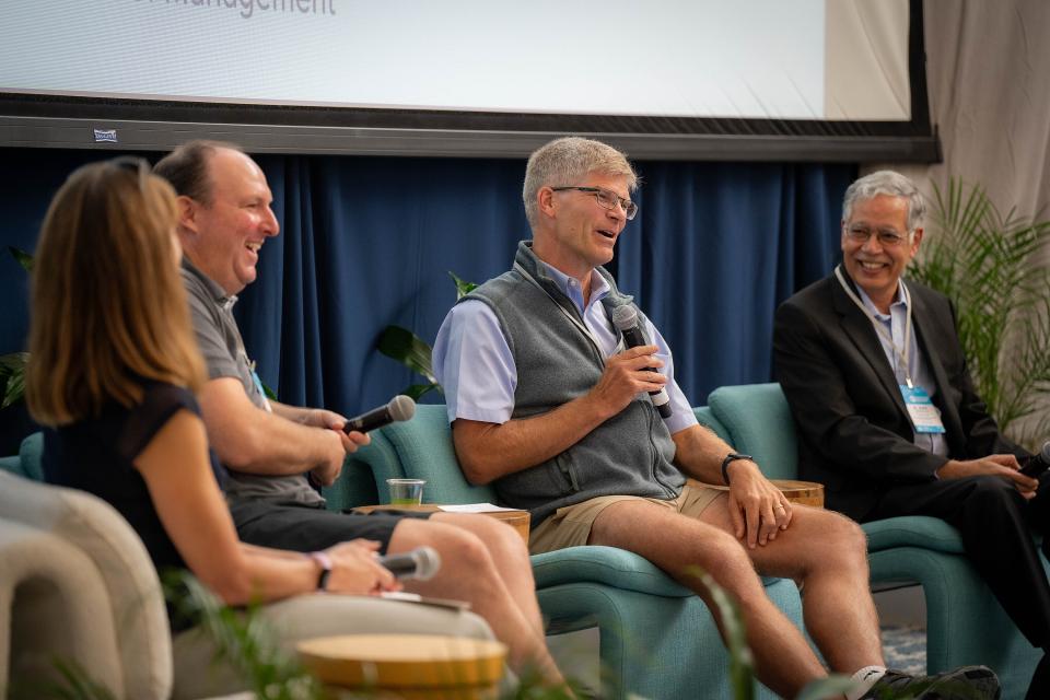 Kim Fisher, Justin Segal, Harold Schmitz, and H. Rao Unnava sitting a panel, holding mics